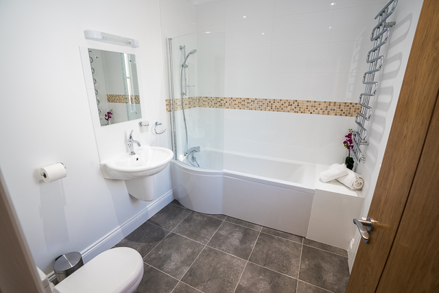 Bathroom located next to downstairs bedroom with shower over bath, sink and toilet